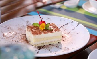 a square dessert with a red flower on top is served on a white plate at Victoria Nui Sam Lodge