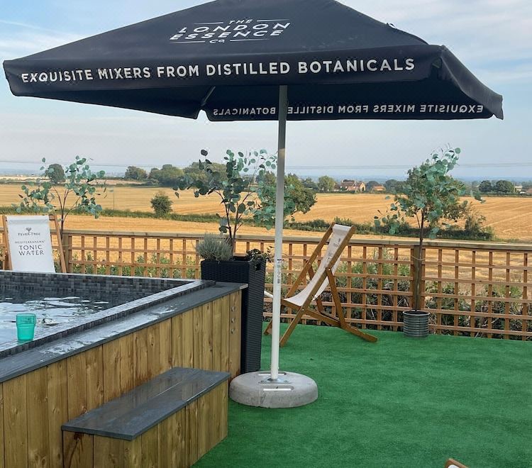 "a black umbrella with a sign advertising "" exquisite mixes from distilled botanicals "" is on display in a grassy area" at The Durham Ox