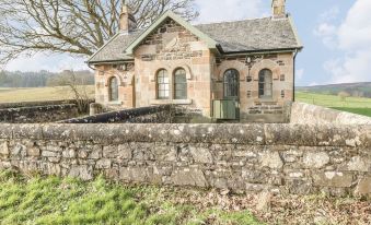 a stone house with a chimney is surrounded by a stone wall and grassy field at Kennels
