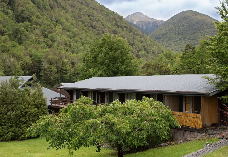 a large wooden house surrounded by trees and mountains , with a balcony and a deck at Maruia Hot Springs