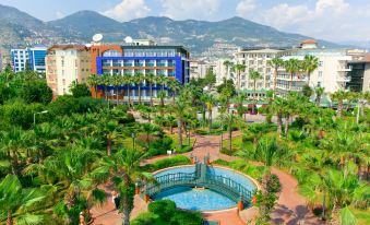 a city park with a large pool surrounded by palm trees , and a building in the background at Gardenia Hotel