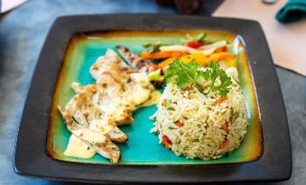 a blue plate with a piece of fish on it , accompanied by a side of rice and vegetables at Siesta Hotel