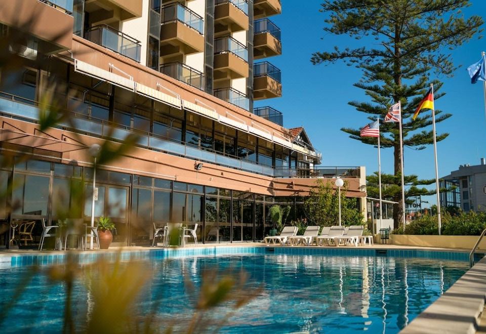 a large swimming pool is surrounded by a hotel building with an american flag flying at Hotel Estoril Eden