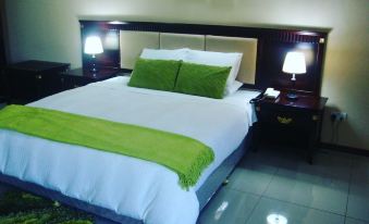 a large bed with a white comforter and green pillows is shown in a hotel room at Riverside Apartments