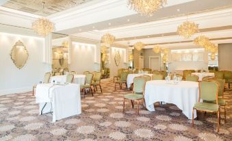 a large dining room with multiple tables and chairs , some of which are covered in white tablecloths at Thornton Hall Hotel & Spa