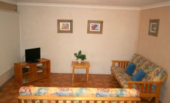 a living room with a wooden floor , two couches , a television , and two pictures on the wall at Lake Edge Holiday Units
