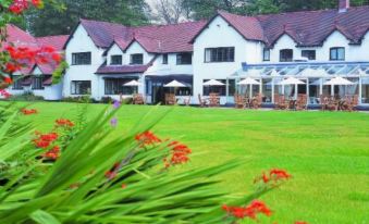 a large white house with a red roof surrounded by lush green grass and flowers at Macdonald Craxton Wood Hotel