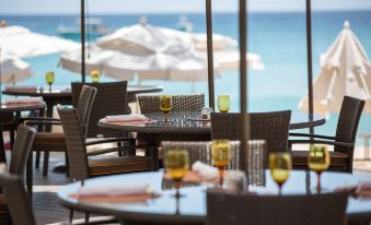 a restaurant with large windows offering an ocean view , dining tables set with wine glasses and orange juices at Colony Club by Elegant Hotels
