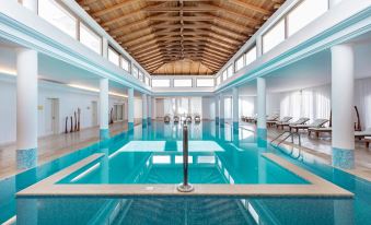 an indoor swimming pool with blue water , surrounded by white walls and a wooden ceiling at Mitsis Selection Laguna