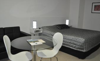 a modern bedroom with a black bed , white walls , and a glass table with two chairs at Keith Motor Inn