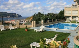 a pool surrounded by a grassy area with several lounge chairs and a view of the ocean at Hotel Miramar Laredo