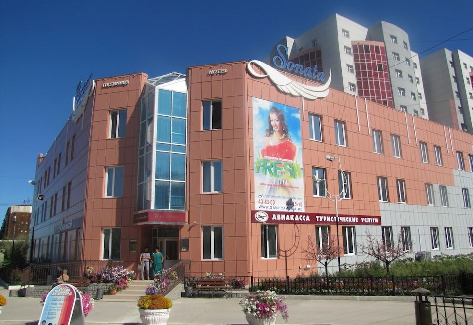 a large brick building with a poster on the side and flowers in front of it at Sonata