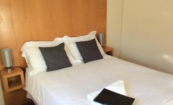 a clean and well - organized bedroom with a white bed , two pillows , and a black book on the bedside table at Coach House Hotel