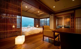 a bedroom with a large bed and chair , wooden floors , and a view of the outside through large windows at Shosenkaku Kagetsu
