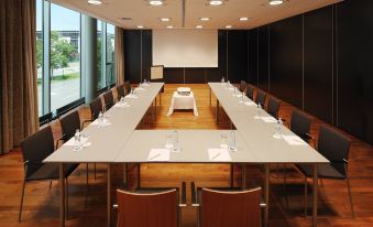 a conference room with a long table , chairs , and various items such as water bottles , papers , and pens at Four Points by Sheraton Panoramahaus Dornbirn