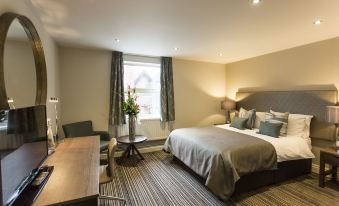 a modern hotel room with a large bed , wooden desk , and window , decorated with green cushions and flowers at Woodland Grange