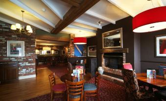 a cozy bar with wooden furniture , a fireplace , and a table for four people to enjoy drinks at Premier Inn Wirral (Greasby)