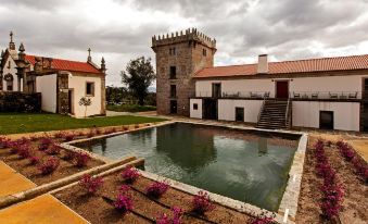 a large pool of water is surrounded by a stone wall and a tower in the background at Torre de Gomariz Wine & Spa Hotel