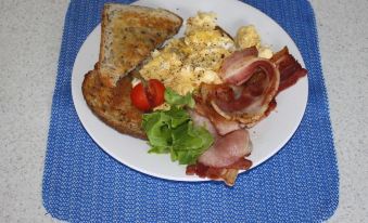 a blue placemat with a plate of food , including scrambled eggs , bacon , and toast , sitting on a white plate at Waterview Motel Maclean
