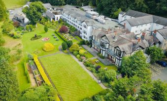 an aerial view of a large , white building with multiple floors and balconies , surrounded by lush green trees and a lush garden at Castle Green Hotel in Kendal, BW Premier Collection