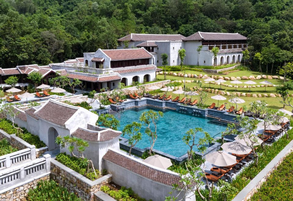 a large white house surrounded by a lush green garden , with a swimming pool in the foreground at Legacy Yen Tu - MGallery