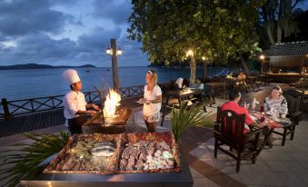 a group of people enjoying a meal at a restaurant , with a view of the ocean in the background at Perhentian Island Resort