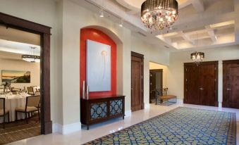 a spacious , well - lit foyer with a large chandelier hanging from the ceiling , surrounded by multiple doors and a carpeted floor at The Pearl Hotel