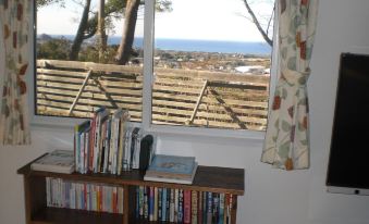 a wooden bookshelf filled with books is positioned in front of a window that offers a view of the ocean at Tea Trees