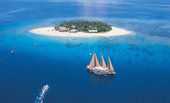 a sailboat is sailing near a small island in the ocean , with a building on the other side at Beachcomber Island Resort