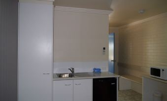 a kitchen with white cabinets , a sink , and a dishwasher is shown next to a bathroom at Emu Park Motel
