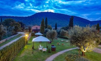a serene outdoor setting with a gazebo , umbrellas , and tables under the setting sun , surrounded by trees and mountains at Abbadia Sicille Relais