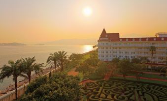 At dusk, the sun sets over a city, revealing its gardens and an ocean in the foreground at Hong Kong Disneyland Hotel