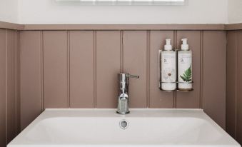 a modern bathroom with brown paneling , white sink , and a silver faucet , along with two bottles of soap on a shelf at The Seven Stars