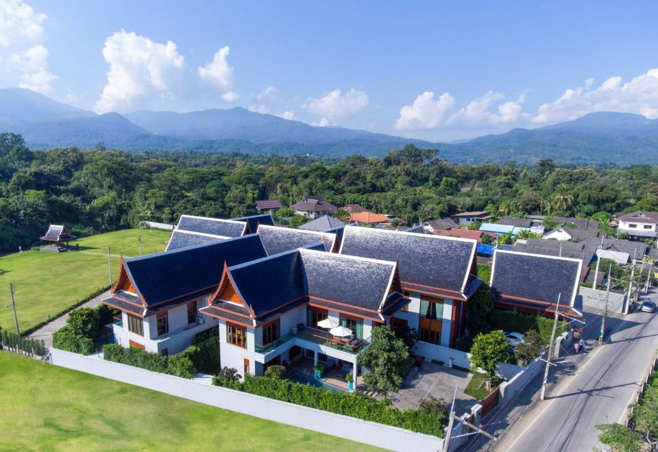 a group of buildings with blue roofs and white walls are surrounded by green grass and trees , set against the backdrop of mountains at Mae Rim Grace
