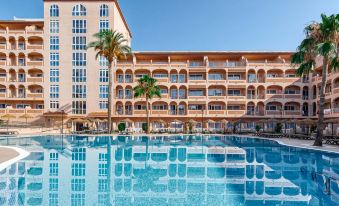 a large swimming pool is surrounded by a hotel building with many balconies and palm trees at Bahia Tropical