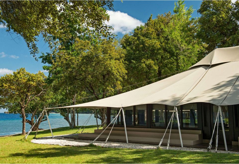 a large white tent is set up in a grassy area near a body of water at Amanwana