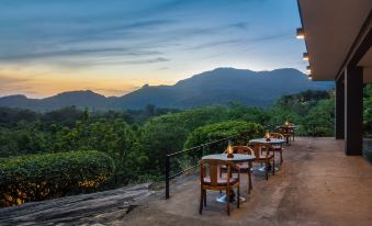 a restaurant with wooden chairs and tables , overlooking a mountainous landscape at sunset , during the day at Heritance Kandalama
