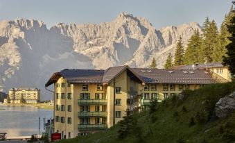 a mountainous landscape with a large building on the side of a hill , surrounded by snow - covered mountains at Grand Hotel Misurina