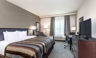 a well - lit hotel room with a large bed , desk , and chair , as well as a window with curtains at Wingate by Wyndham Angola
