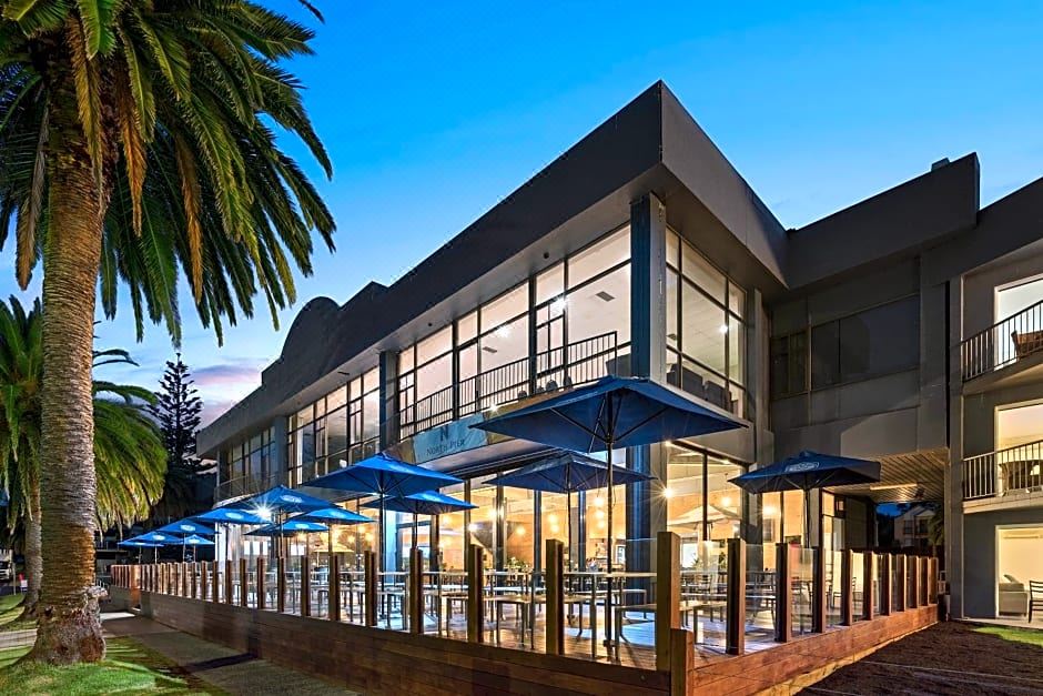a modern building with large glass windows and blue umbrellas in front of a tree at North Pier Hotel