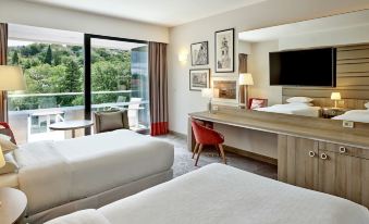 a hotel room with two beds , a desk , and a large window overlooking a garden at Sheraton Dubrovnik Riviera Hotel