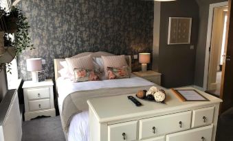 a well - decorated bedroom with a white bed , dresser , and nightstand , along with a tv on the dresser at The Wheatsheaf Pub, Kitchen & Rooms