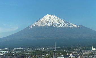 a snow - covered mount fuji in the background , with a city and buildings in the foreground at Hotel Route-Inn Fuji Chuo Koen Higashi