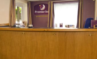 a reception desk with a purple sign on the wall and windows in the background at Premier Inn Tring
