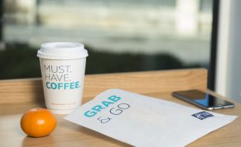 "a cup of coffee and an orange are on a table with a paper that says "" must have coffee "" next to an orange" at Holiday Inn Express Stafford