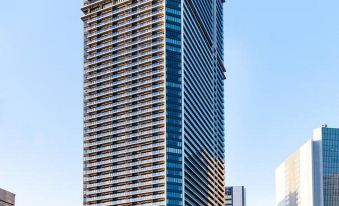 a tall skyscraper with a unique design and glass windows stands against a clear blue sky at Oakwood Suites Yokohama