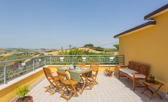 a sunny terrace with wooden furniture , including chairs and a table , overlooking a landscape of rolling hills and clear blue skies at Erika