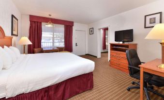 a hotel room with a bed , desk , and tv , along with red curtains and a window at The Classic Desert Aire Hotel