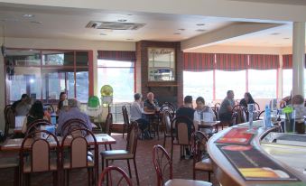 a group of people sitting at tables in a restaurant with red chairs and windows at Beauty Point Waterfront Hotel