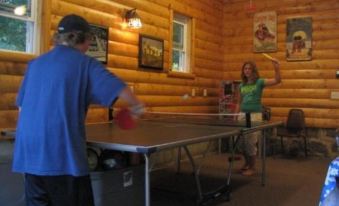 a group of people , including a man and a woman , are playing table tennis in a wooden cabin at Riverside Resort